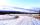 Une route de campagne couverte de neige; on voit des montages au loin.